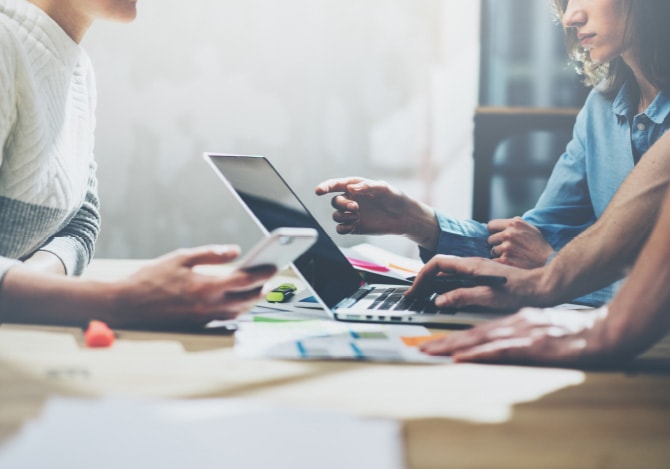 パソコンとスマートフォンを持って話し合う男女